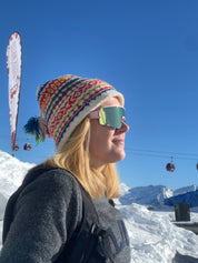 Person wearing a colorful knit hat and sunglasses with a snowy landscape and ski lift in the background
