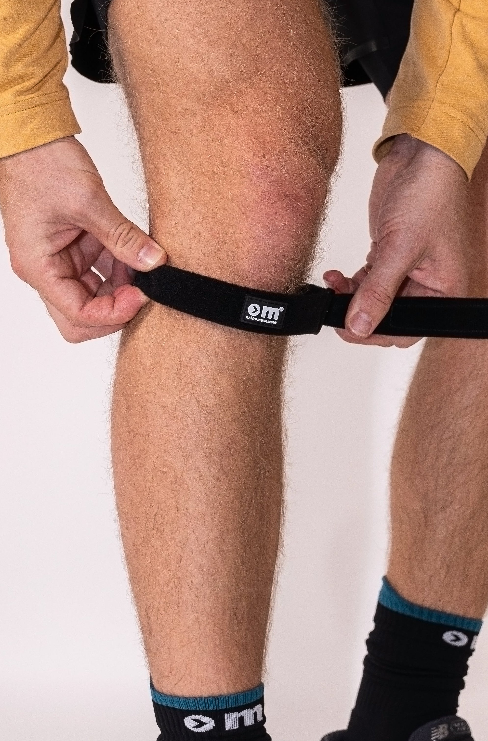 Person wearing a knee strap, black socks and black athletic shoes with a white background