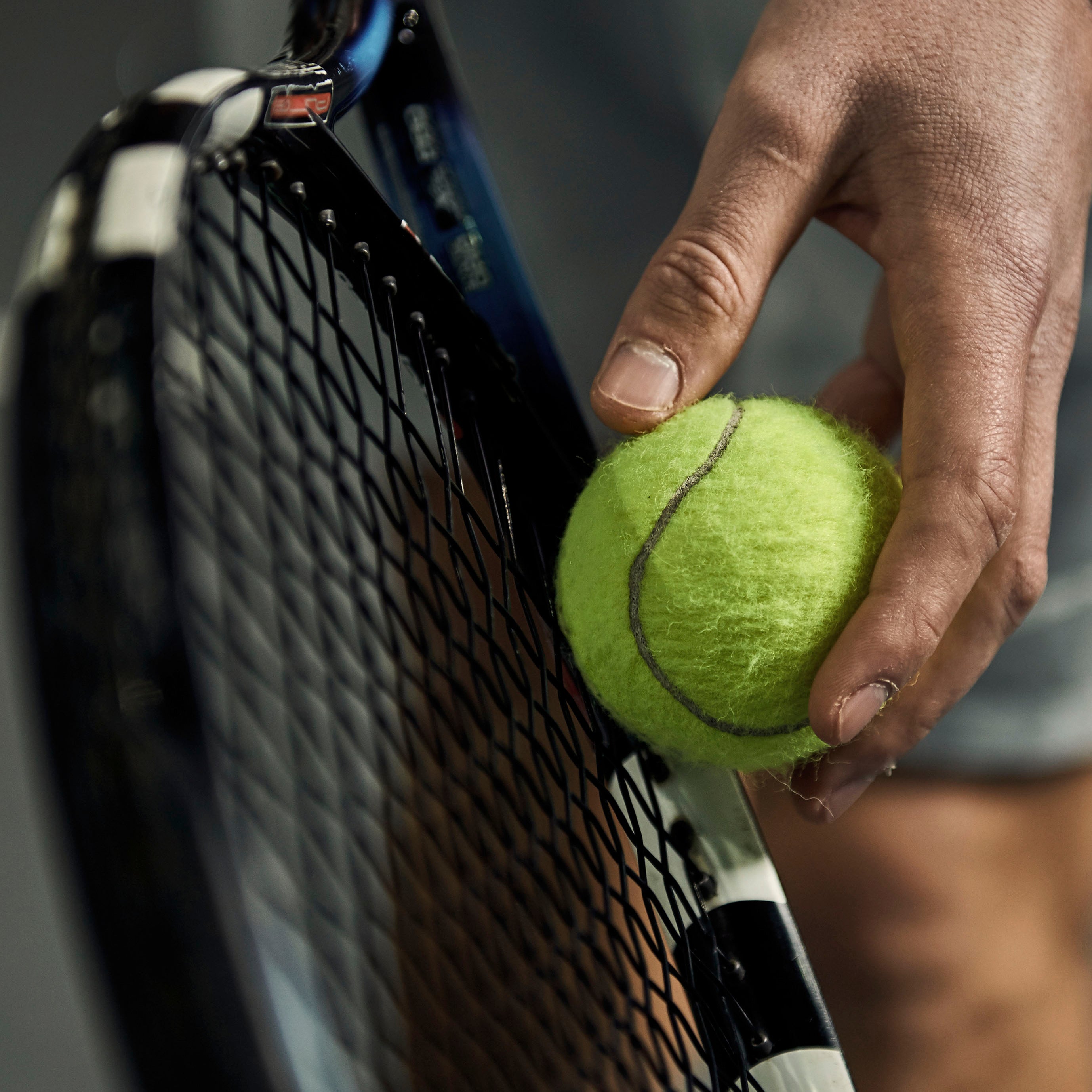 Hand holding a tennis ball next to a tennis racket on a blurred background