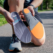 Person holding a pair of gray and orange insoles outdoors.